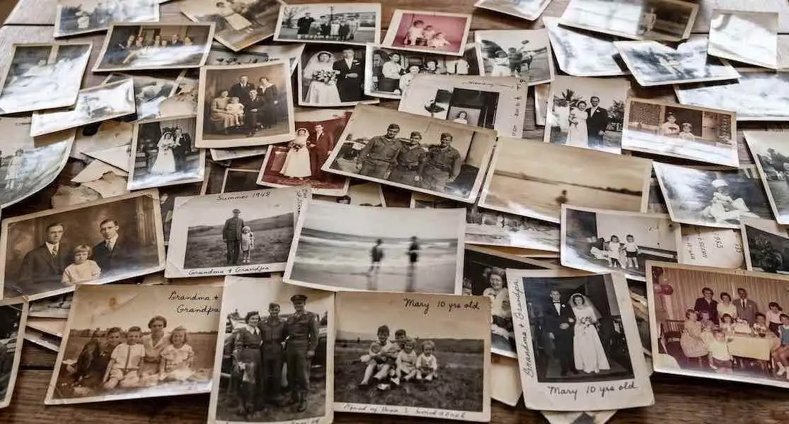 A collage of dozens of vintage black and white family photographs scattered on a table, symbolizing the bulk image upload feature for AI heritage video creation.